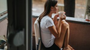 A,Young,Woman,Sits,On,A,Balcony,With,A,Warm